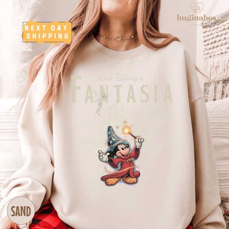 A woman wearing a white sweatshirt with a Disney character and text printed on it.