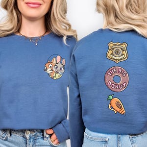 A woman wearing a blue sweater with cartoon characters and a police badge on the back.