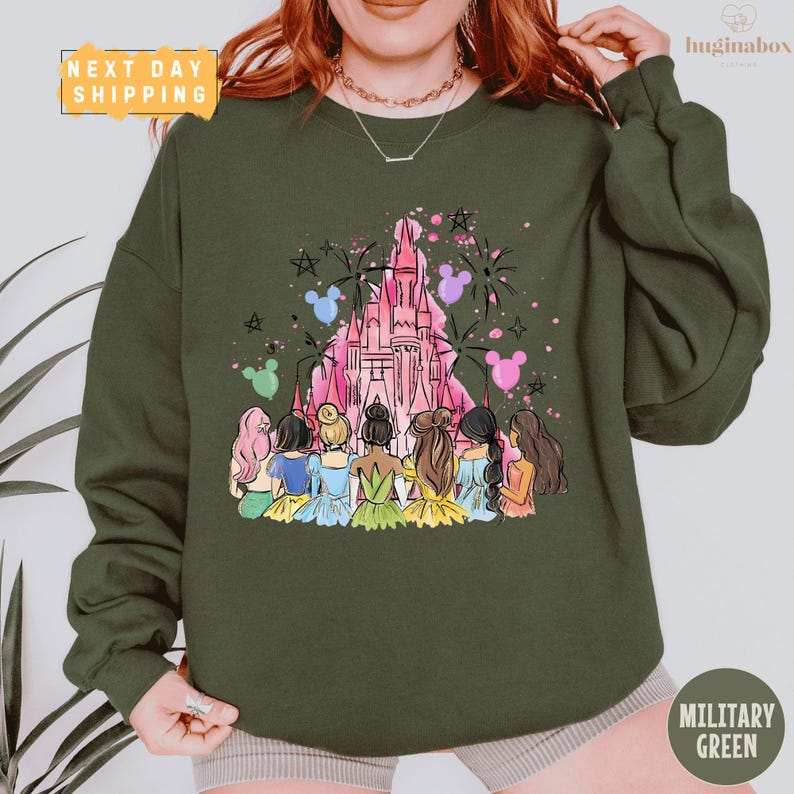 A woman wearing a green sweatshirt with a colorful illustration of Disney princesses and a castle on it.