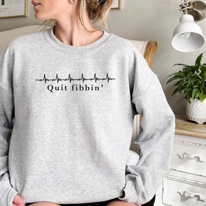 a woman sitting on a bed wearing a grey sweatshirt