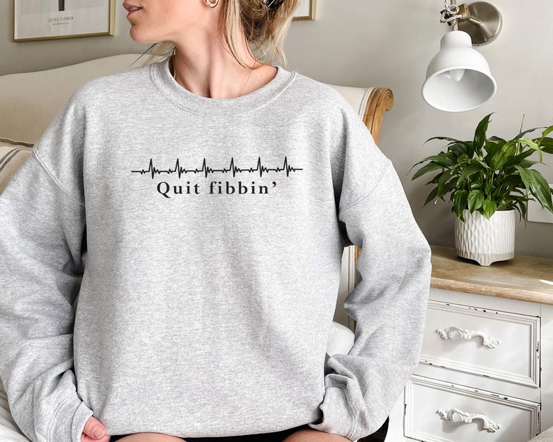a woman sitting on a bed wearing a grey sweatshirt