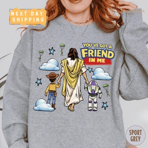 A gray sweatshirt with a cartoon illustration of a woman holding a child and a character from the Toy Story franchise, along with the text "You've got a FRIEND in ME" and a "Next Day Shipping" label.