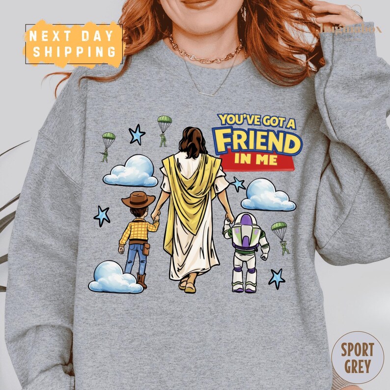 A gray sweatshirt with a cartoon illustration of a woman holding a child and a character from the Toy Story franchise, along with the text "You've got a FRIEND in ME" and a "Next Day Shipping" label.