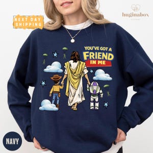 A navy blue sweatshirt with a graphic design depicting a woman in a yellow dress and a child, along with a character resembling a robot or space-themed character. The text on the sweatshirt reads "You've got a FRIEND in ME".