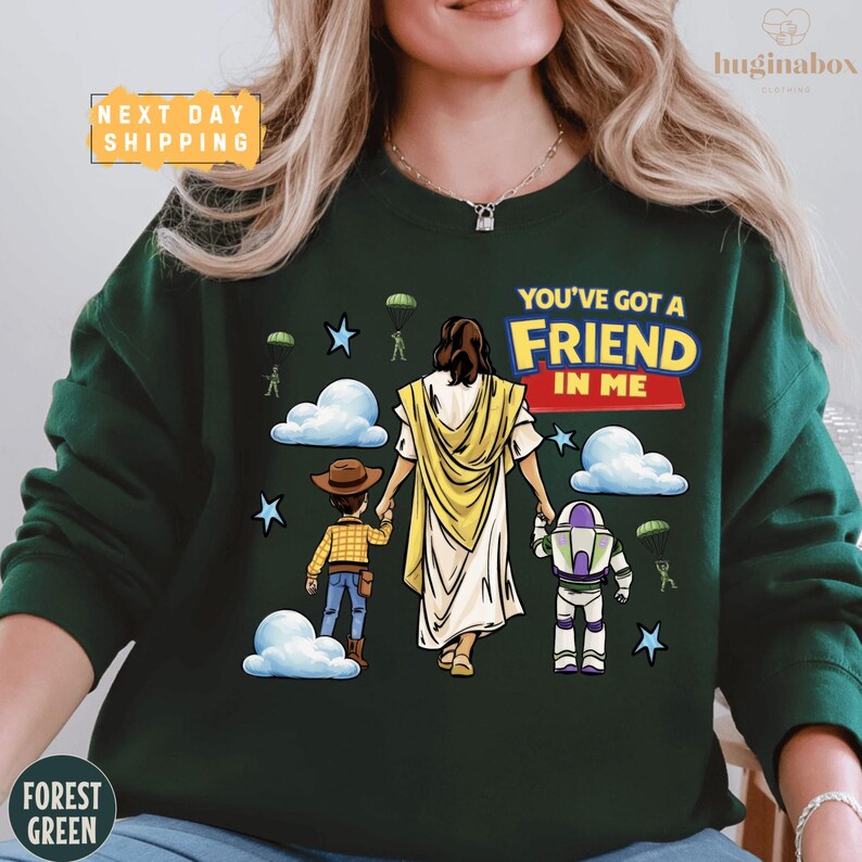 A woman wearing a green sweatshirt with a graphic design depicting a cartoon-style illustration of Jesus Christ holding a child and a character from the Toy Story franchise.