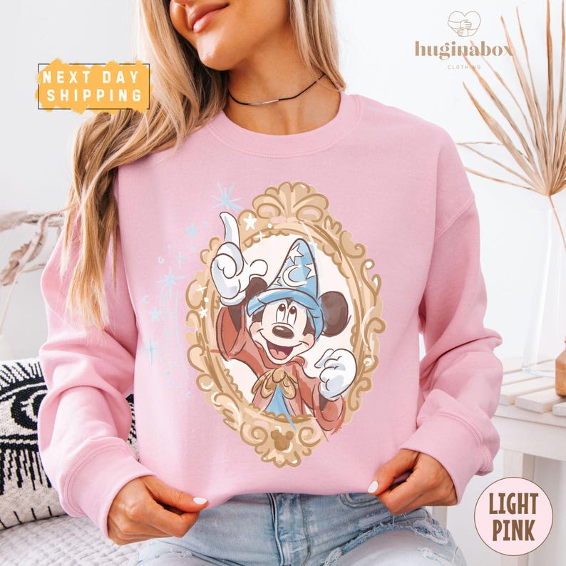A woman wearing a pink sweatshirt with a Mickey Mouse design is shown in the image.
