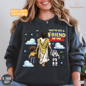 A woman wearing a gray sweatshirt with a graphic design depicting a cartoon depiction of Jesus Christ surrounded by various characters, including a boy and a dog.