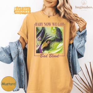 A woman wearing a yellow t-shirt with a graphic design featuring a character from the Disney movie "Bad Blood".