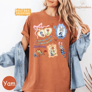 A woman wearing a t-shirt with a cartoon character design, including a rabbit, a heart, and other cartoon-style elements. She is also wearing a denim jacket and has her arms around her shoulders.