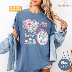 A woman wearing a blue t-shirt with a graphic design featuring a character from the video game series Yoshi.