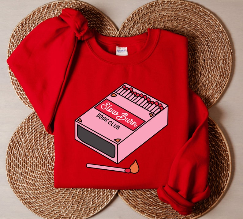 May include: Red sweatshirt with a graphic of a pink matchbox with the text "Slow Burn Book Club".