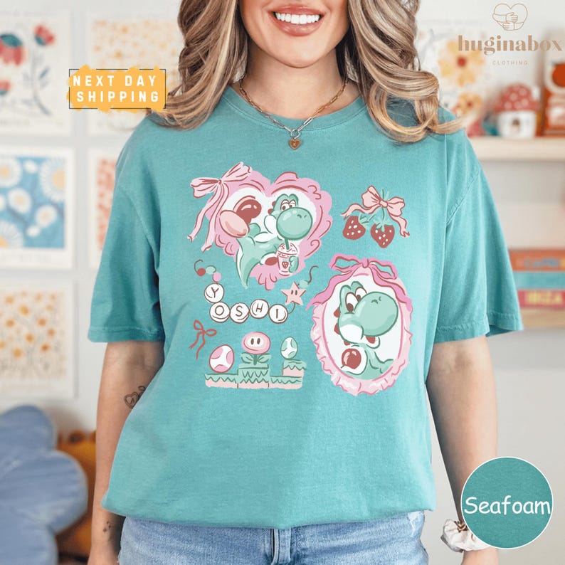 A woman wearing a teal t-shirt with a colorful graphic design featuring characters from the Mario video game franchise.