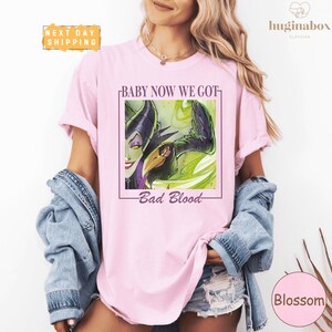 A woman wearing a pink t-shirt with a graphic design and text, standing against a white background.