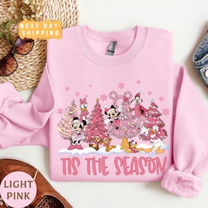 May include: Pink Christmas sweatshirt with a design of Mickey Mouse, Minnie Mouse, Donald Duck, Goofy, and Pluto wearing Santa hats and holding Christmas trees. The text "Tis the Season" is printed below the design.