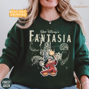 A woman wearing a green sweatshirt with a Disney-themed design, including a character and a castle.
