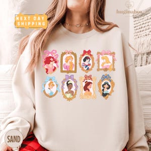 A woman wearing a white sweatshirt with a graphic of various Disney princesses in frames.