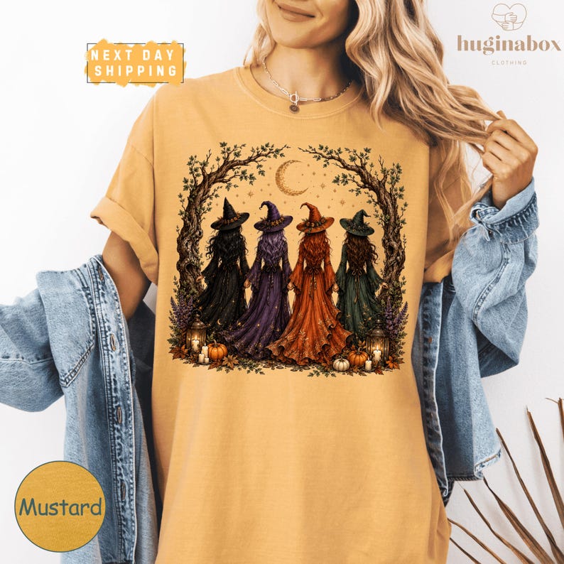 A woman wearing a yellow t-shirt with a graphic design of four women dressed in witch costumes standing in a circle under a crescent moon and stars.