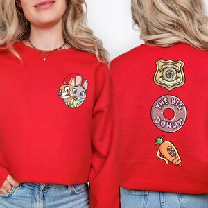 A woman wearing a red sweatshirt with cartoon characters and text on the back.