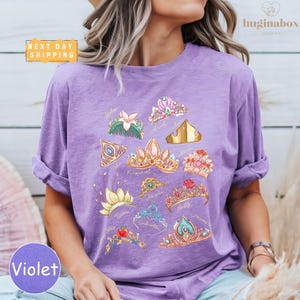 A woman wearing a purple t-shirt with a graphic design of various crowns and jewels printed on it.