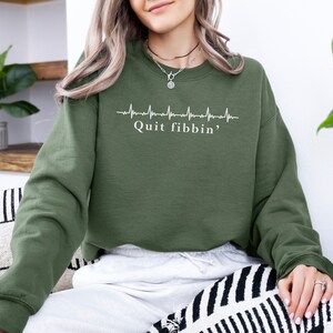 a woman sitting on a couch wearing a green sweatshirt