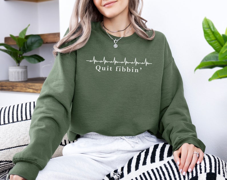 a woman sitting on a couch wearing a green sweatshirt