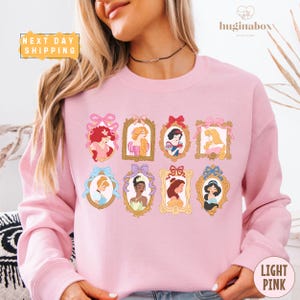 A woman wearing a pink sweatshirt with a design of various Disney princesses in frames.