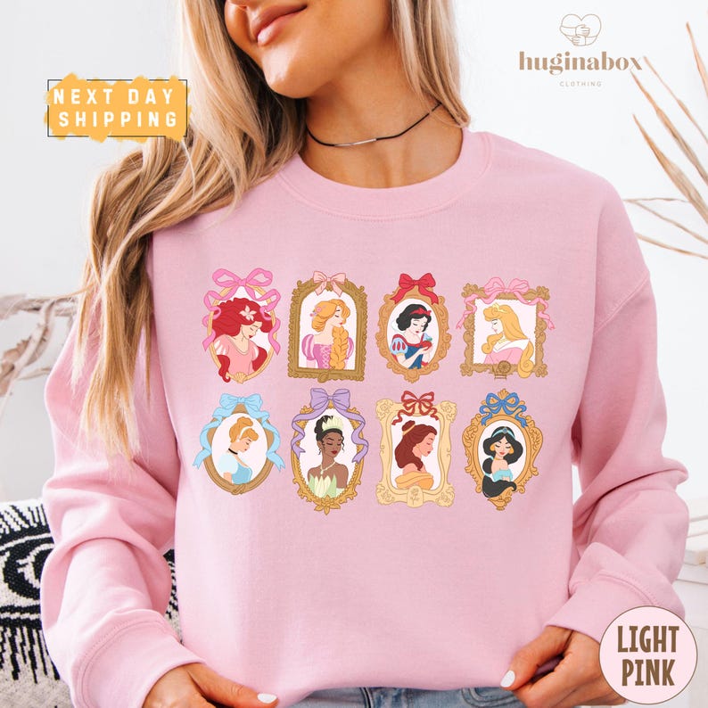 A woman wearing a pink sweatshirt with a design of various Disney princesses in frames.