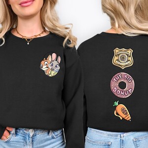 A woman wearing a black sweater with cartoon characters and a police badge on the back.