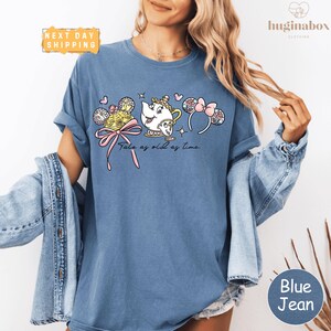 A woman wearing a blue t-shirt with a cartoon character and text printed on it, along with a denim jacket.