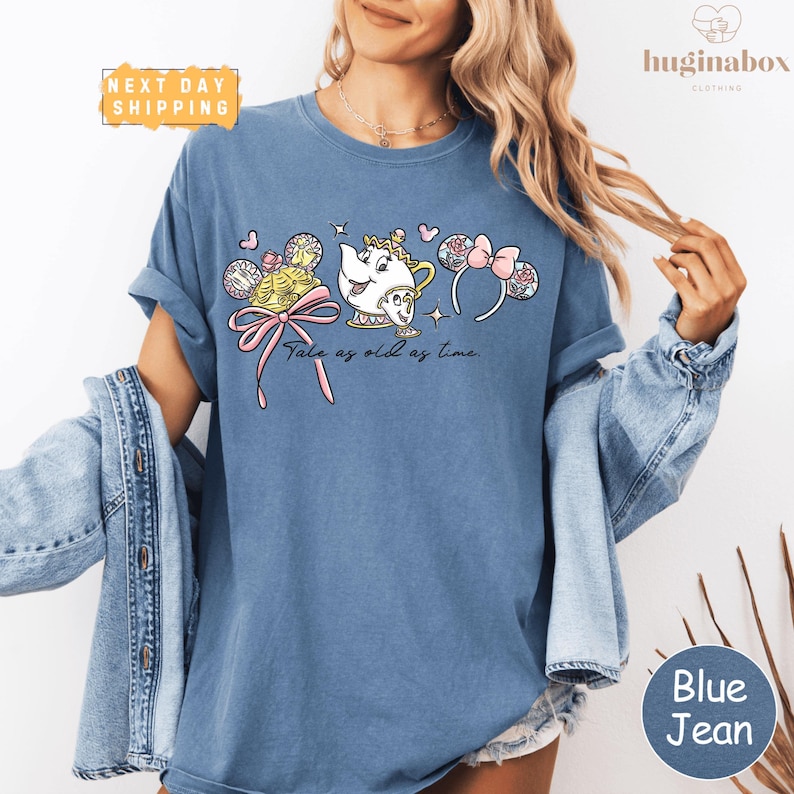 A woman wearing a blue t-shirt with a cartoon character and text printed on it, along with a denim jacket.