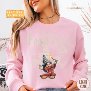 A woman wearing a pink sweatshirt with a cartoon character and text printed on it.