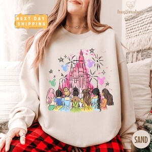 A woman wearing a white sweatshirt with a colorful illustration of a castle and a group of women in various outfits.