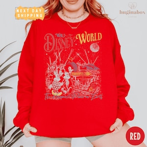 A person wearing a red sweatshirt with a Disney World-themed graphic printed on it.