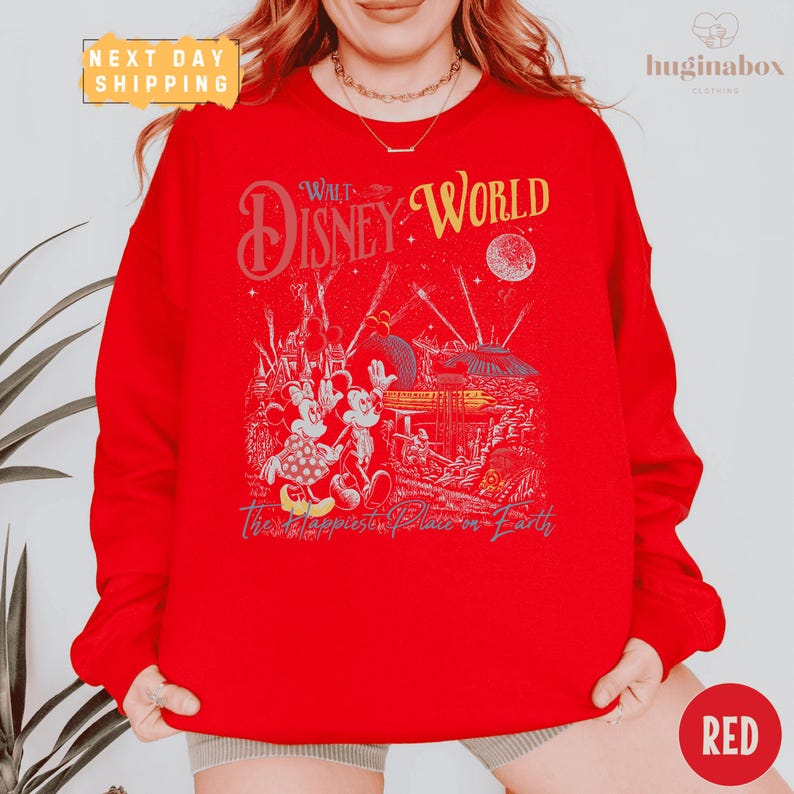A person wearing a red sweatshirt with a Disney World-themed graphic printed on it.