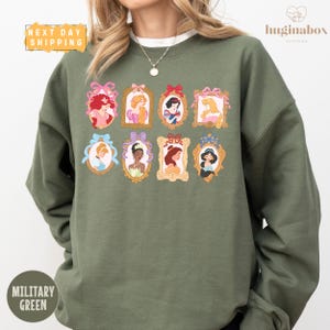 A woman wearing a green sweatshirt with a collage of illustrations of Disney princesses.