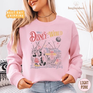 A woman wearing a pink sweatshirt with a Disney World-themed graphic printed on it.