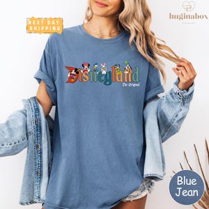 A woman wearing a blue t-shirt with the Disney logo and text, along with a denim jacket, posing against a white background.