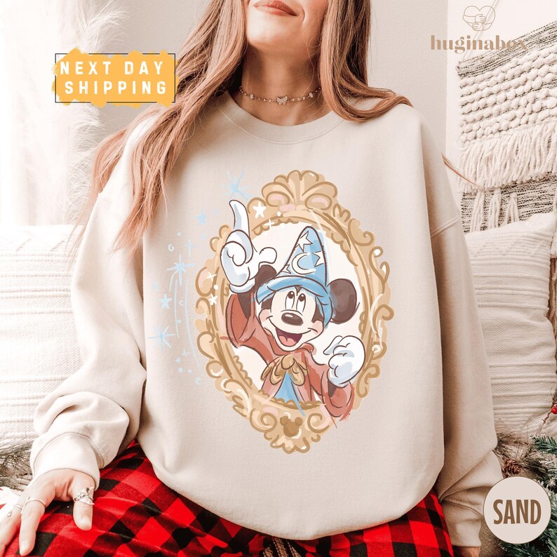 A woman wearing a white sweatshirt with a Mickey Mouse design and a framed illustration of a wizard.