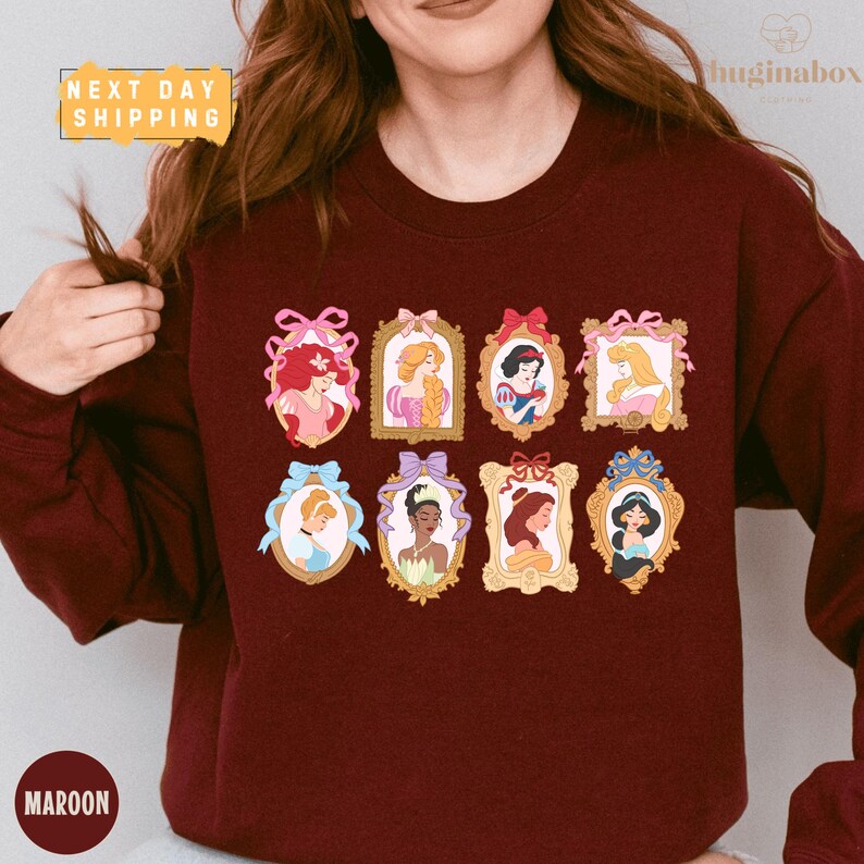 A woman wearing a burgundy sweater with a collage of illustrations of Disney princesses on it.