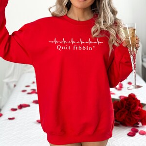 a woman in a red sweatshirt holding a glass of champagne