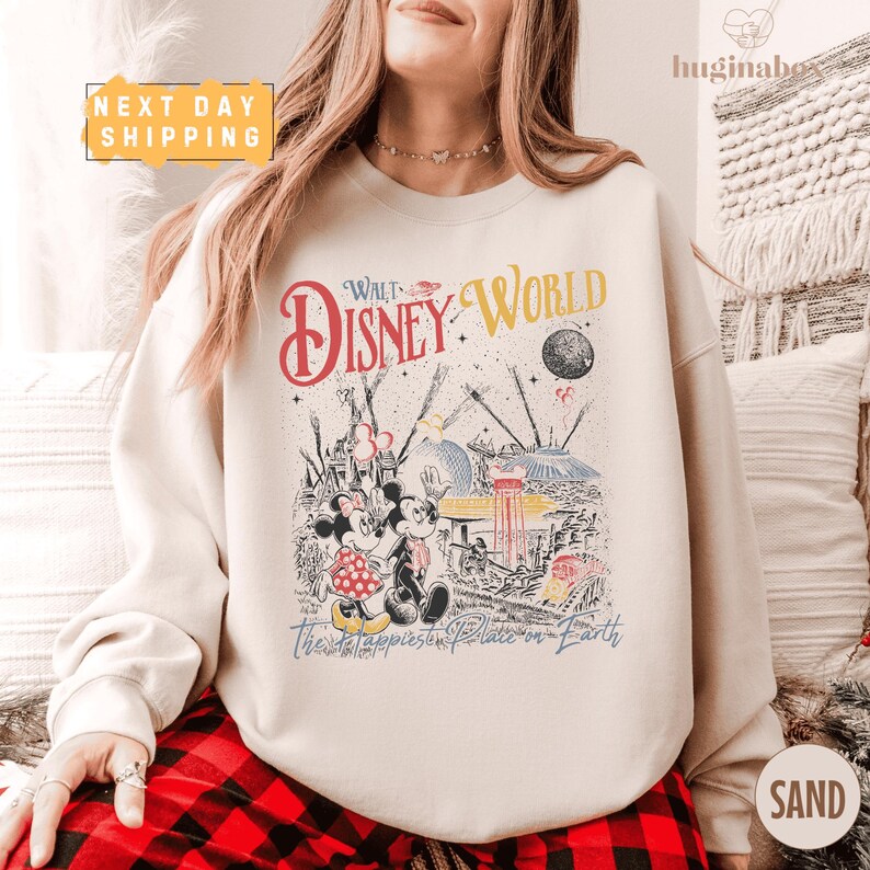 A woman wearing a white sweatshirt with a Disney World-themed graphic printed on it, sitting on a couch.