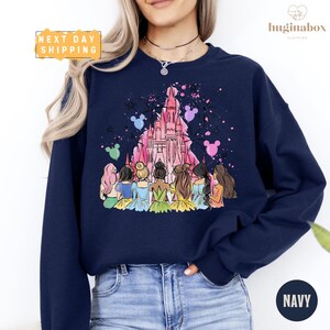 A woman wearing a navy blue sweatshirt with a colorful illustration of a group of women in a castle-like setting.