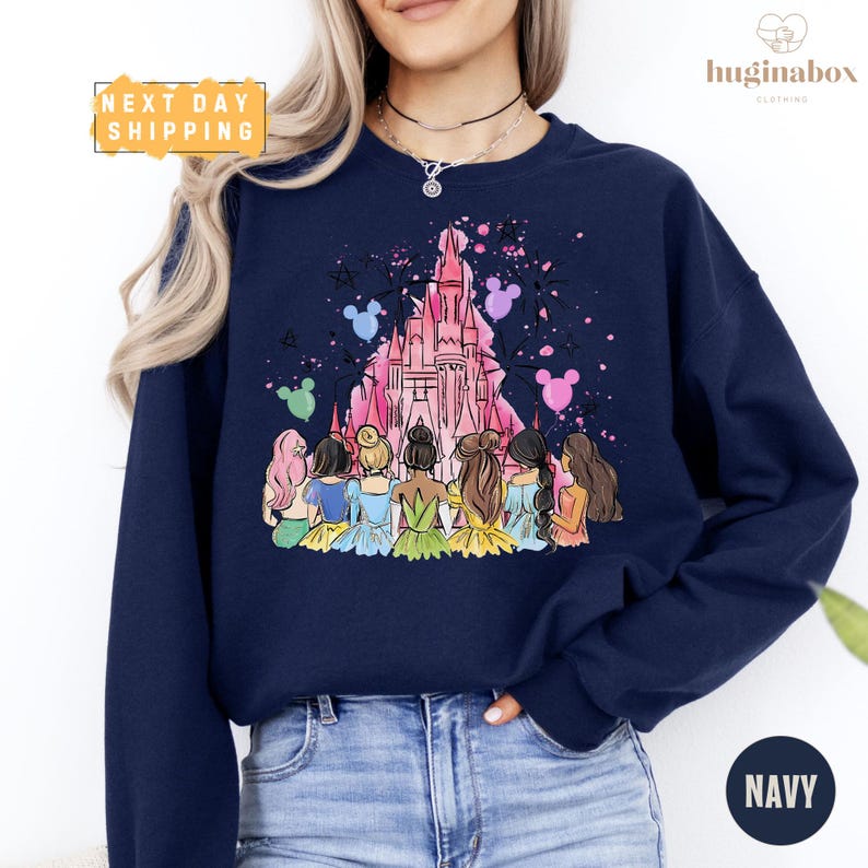 A woman wearing a navy blue sweatshirt with a colorful illustration of a group of women in a castle-like setting.