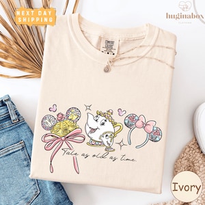 a white t-shirt with a printed design of a character from the Disney film "Beauty and the Beast", along with various accessories such as a teapot, a pair of earrings, and a headband. The text on the t-shirt reads "Tale as old as time".