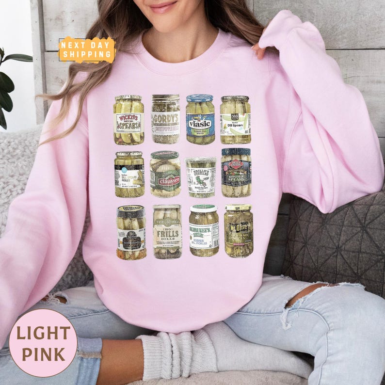 a woman sitting on a couch wearing a pink sweatshirt with a jar of pickles