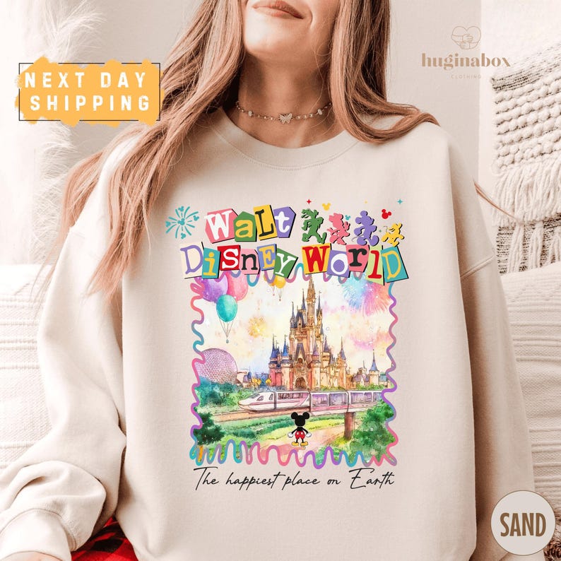 A woman wearing a white sweatshirt with a colorful illustration of Walt Disney World and the text "The happiest place on Earth" printed on it.