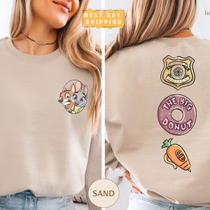 a woman wearing a beige sweater with various cartoon-style logos and designs on the back.