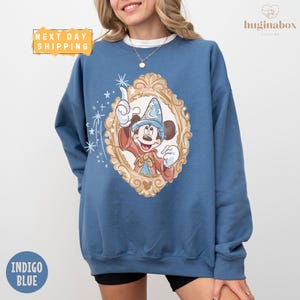 A woman wearing a blue sweatshirt with a Mickey Mouse design and a framed picture of Mickey Mouse.