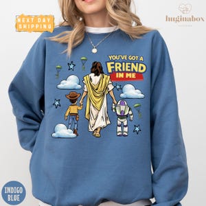 A blue sweatshirt with a cartoon illustration of a person holding a Bible and two children, along with the text "You've got a FRIEND in me" and a Bible character.