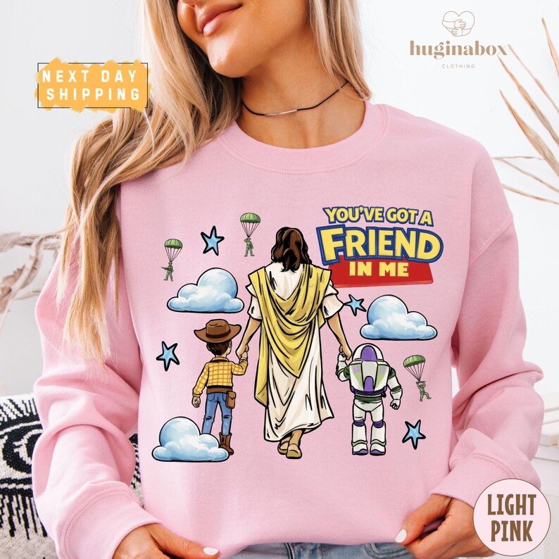 A woman wearing a pink sweatshirt with a cartoon illustration of a man and a child, along with a Bible verse and a character from the Toy Story franchise.